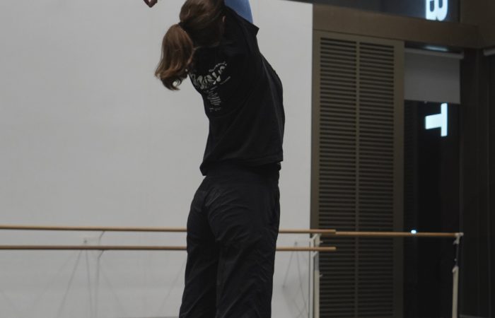 Dancer reaches arms above head in a dance studio.