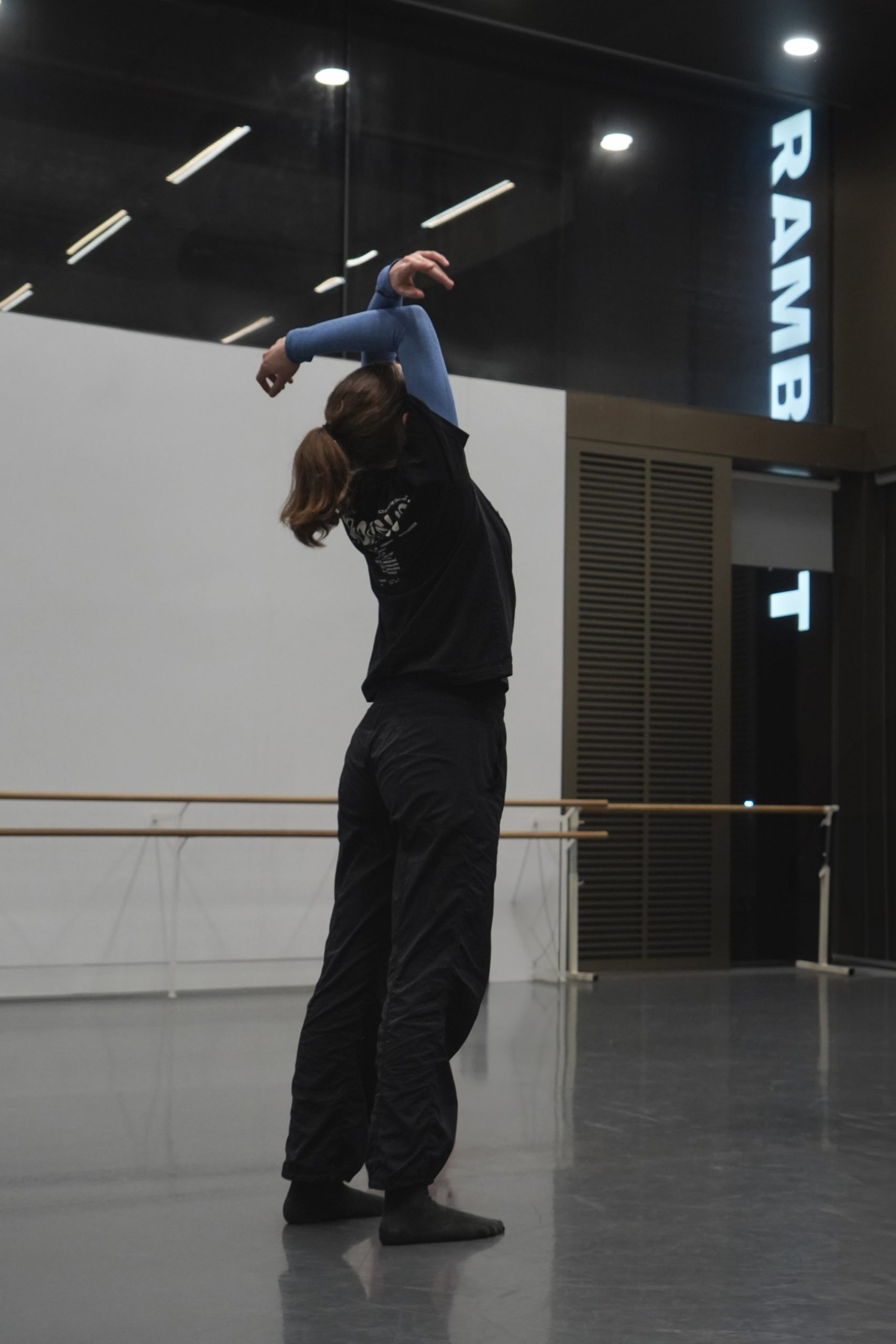 Dancer reaches arms above head in a dance studio.